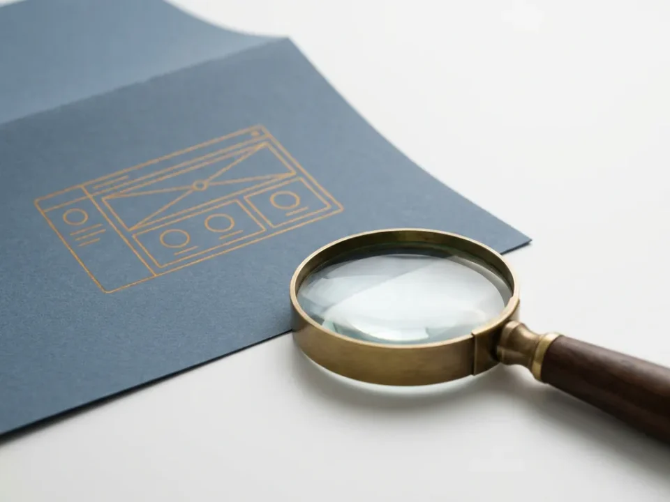 Vergrootglas naast een geometrisch dashboard-wireframe op mat papier, op een wit bureau met leisteenblauw en amber tinten.